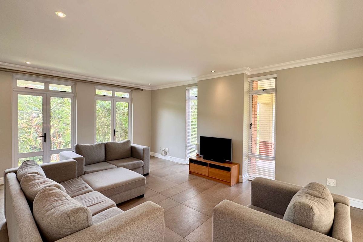A bright and spacious living room featuring neutral tiled flooring, recessed downlights, and multiple sets of french doors providing ample natural light.