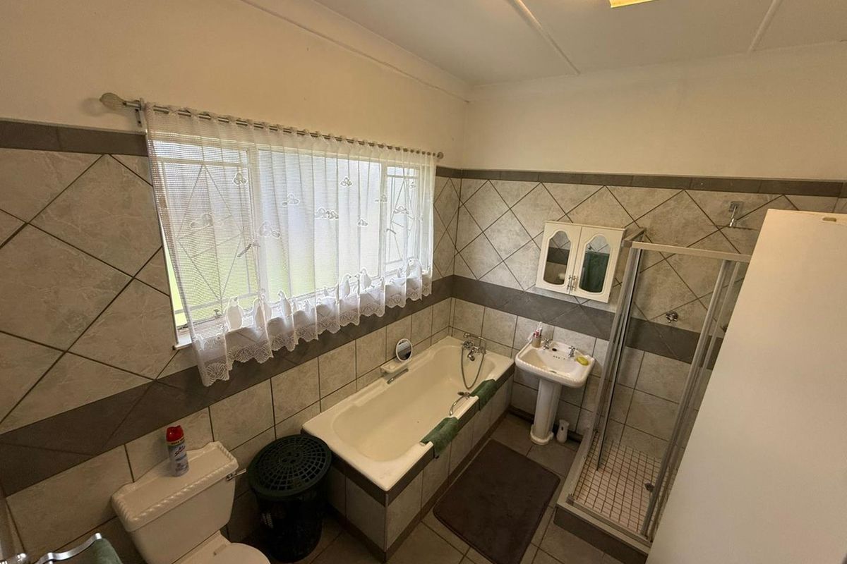 A functional bathroom featuring a bathtub, separate shower enclosure, pedestal basin, and toilet with neutral wall tiling.