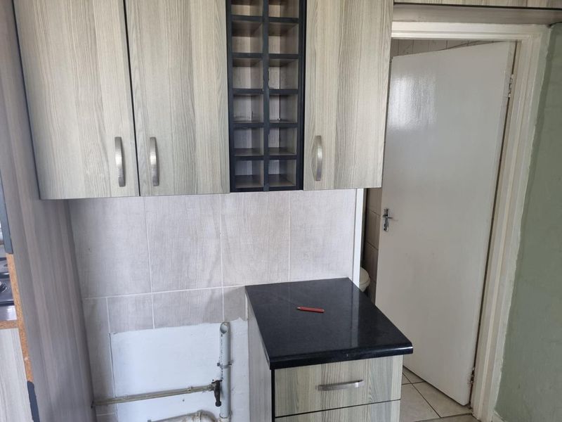 A kitchen area featuring wood-look laminate cabinetry, a black granite countertop, and a tiled backsplash, with visible plumbing connections requiring finishing.