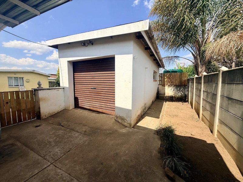 A detached single garage with a roller shutter door, concrete driveway, and surrounding precast boundary walls in a residential backyard setting.