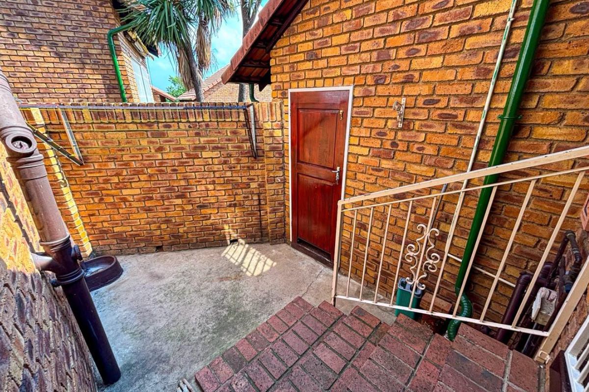 A private rear courtyard area featuring face brick walls, concrete flooring, and a set of brick steps with a metal handrail.