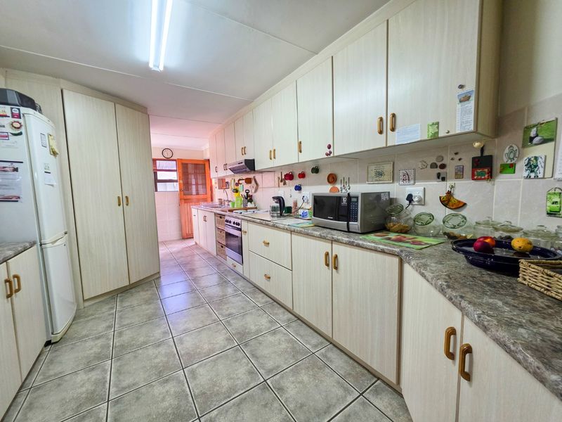 A functional kitchen featuring light-toned laminate cabinetry, stone-look countertops, tiled flooring, and a tiled backsplash with integrated oven and extractor fan.