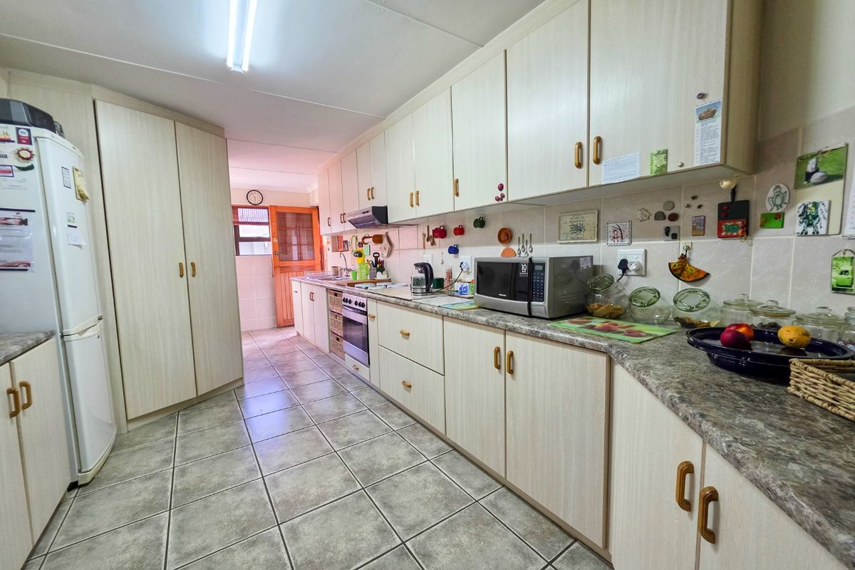 A functional kitchen featuring light-toned laminate cabinetry, stone-look countertops, tiled flooring, and a tiled backsplash with integrated oven and extractor fan.