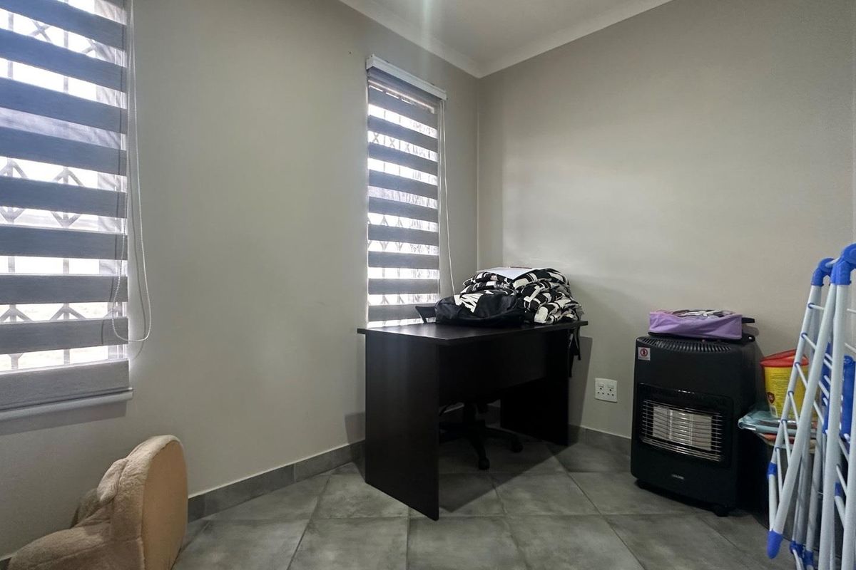 A functional bedroom or office space featuring tiled flooring, dual windows with modern roller blinds, and neutral wall finishes.