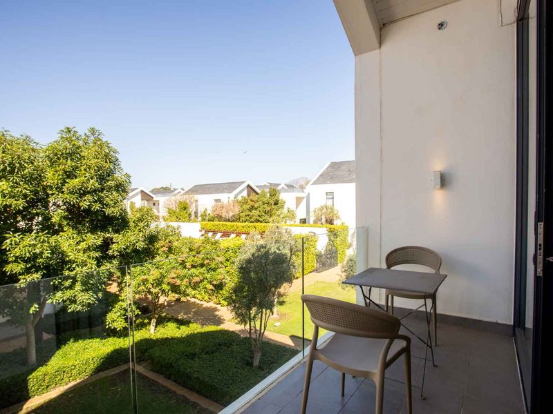 A private balcony featuring a modern glass balustrade and tiled flooring, overlooking a well-maintained communal garden area.