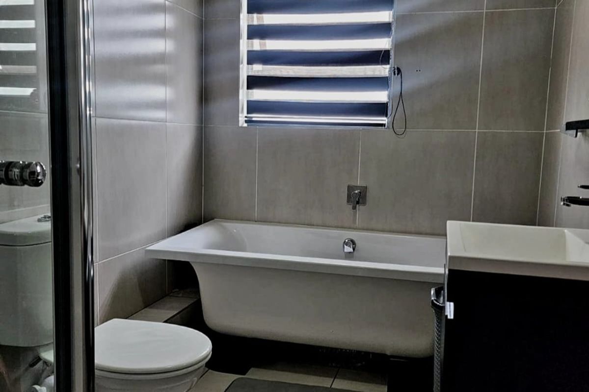 Modern bathroom featuring a freestanding bathtub, wall-mounted faucet, ceramic toilet, and a vanity basin with neutral wall and floor tiling.