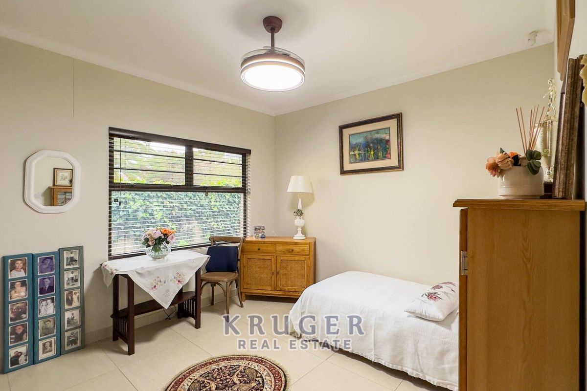 A well-maintained bedroom featuring neutral tiled flooring, a large window with aluminium frames, and a central ceiling light fixture.