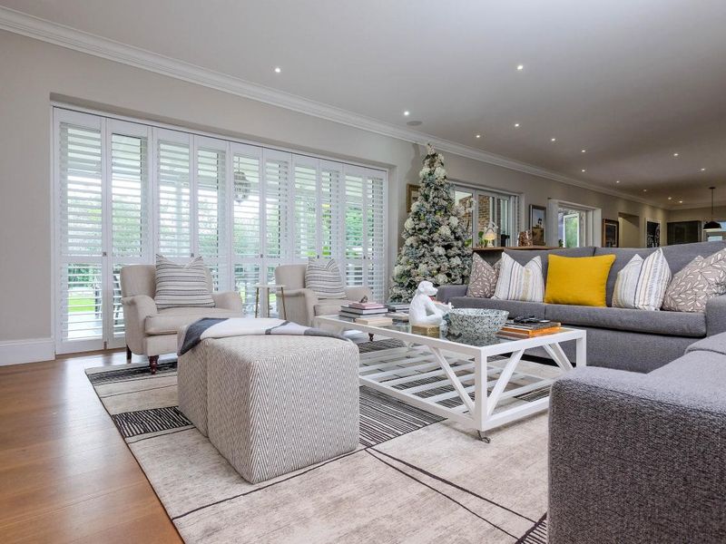 Spacious living room featuring hardwood flooring, recessed downlights, crown molding, and large plantation shutters providing ample natural light.