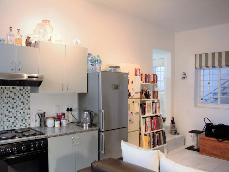 Open plan kitchen area featuring built-in cabinetry, granite countertops, tiled splashback, and integrated cooking appliances, adjacent to a living space with security-barred windows.