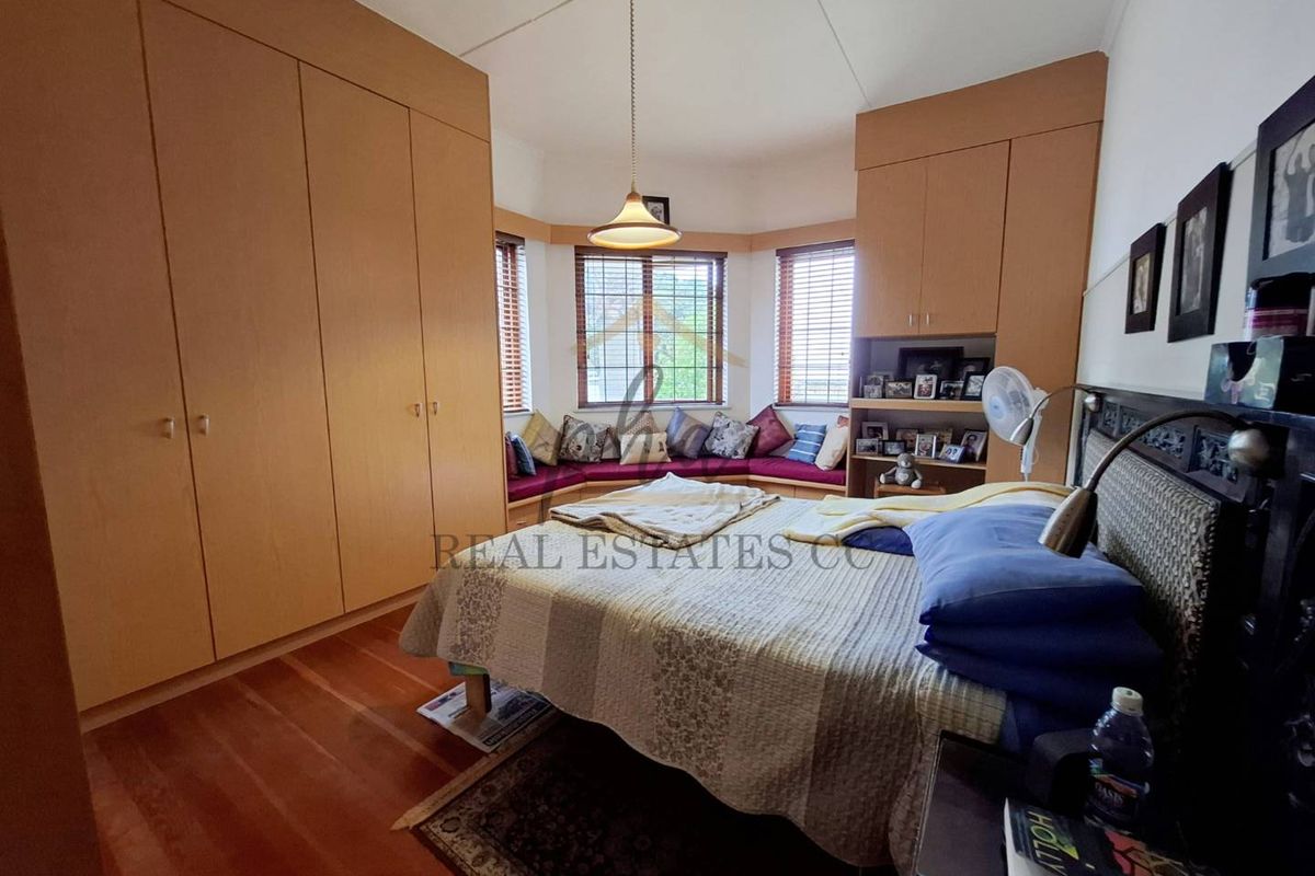 A bedroom featuring extensive built-in wooden cabinetry, a bay window with integrated seating, and warm timber flooring.