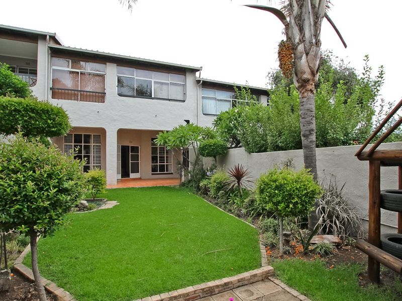 Rear view of the townhouse featuring a private garden, lawn, paved walkway, and a covered patio area with access through sliding doors.