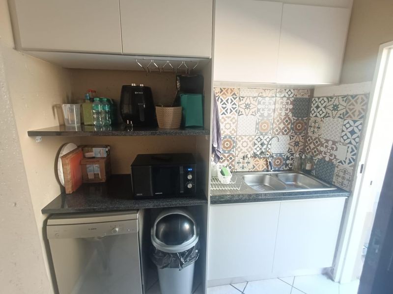 A functional scullery area featuring granite countertops, a double bowl sink, patterned tile splashback, and built-in cabinetry with space for a dishwasher.
