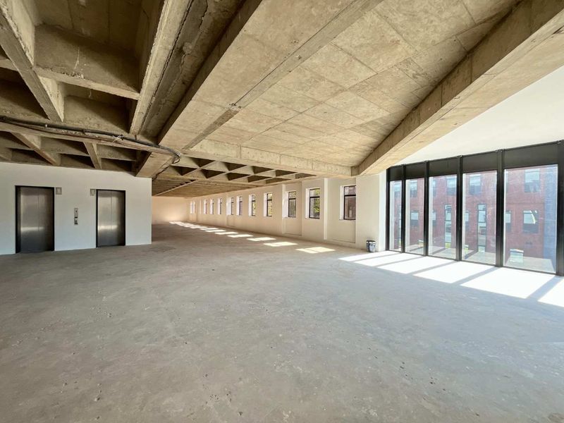 Expansive open-plan office space featuring an exposed concrete waffle ceiling, floor-to-ceiling windows, and dual elevator access, currently in shell condition.