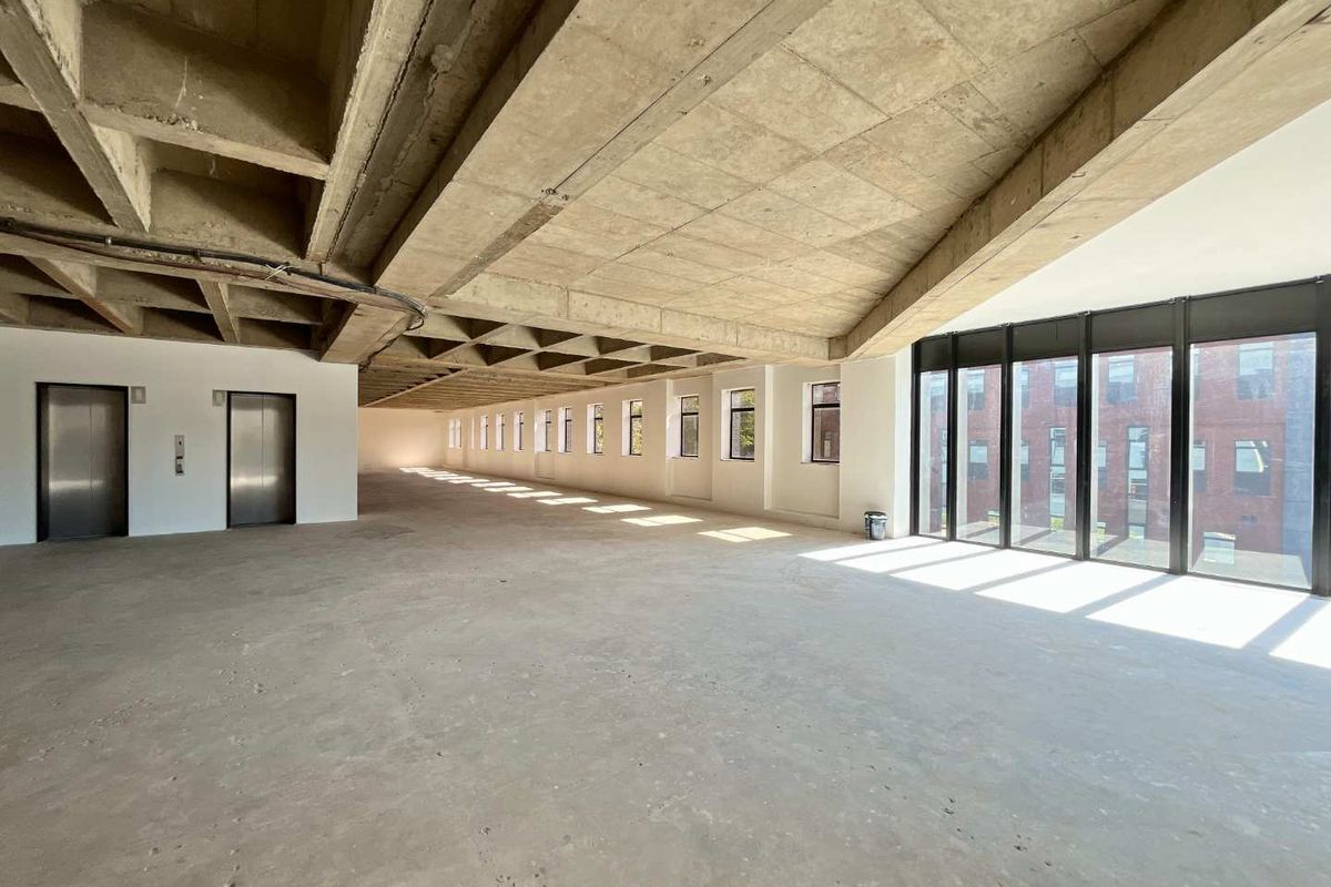 Expansive open-plan office space featuring an exposed concrete waffle ceiling, floor-to-ceiling windows, and dual elevator access, currently in shell condition.