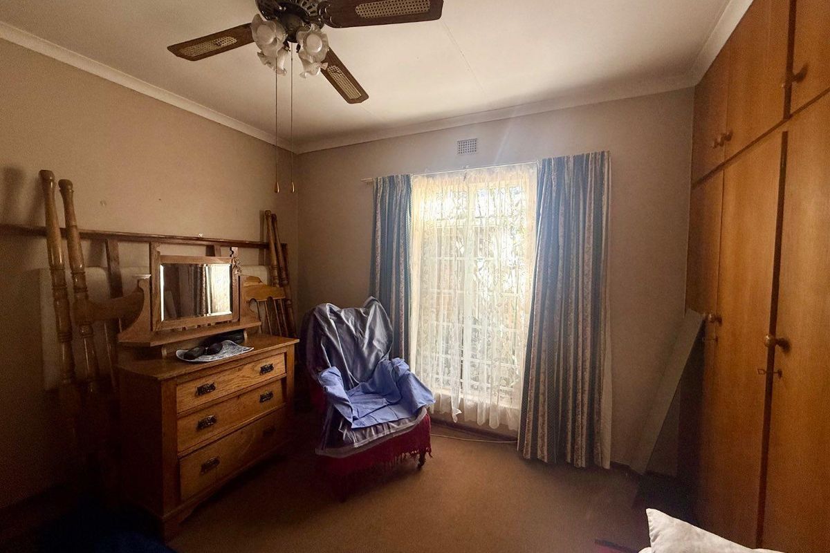 A bedroom featuring built-in wooden cupboards, a ceiling fan, and carpeted flooring, offering a functional space with potential for modernization.