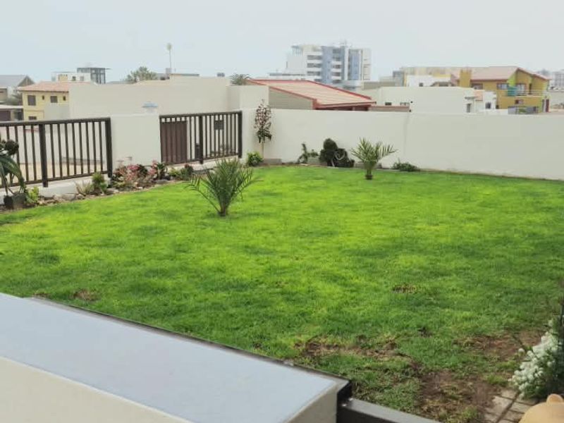 A well-maintained private garden featuring a lush green lawn, paved walkway, and secure boundary walls with metal railings.