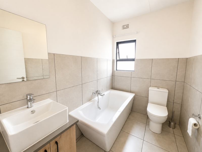 Modern bathroom featuring a vanity with basin, a bathtub, and a toilet, finished with neutral wall and floor tiles.
