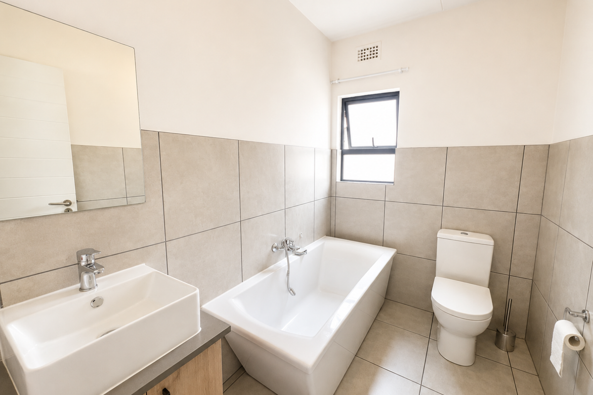 Modern bathroom featuring a vanity with basin, a bathtub, and a toilet, finished with neutral wall and floor tiles.