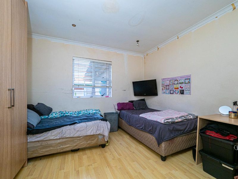 A bedroom featuring laminate flooring, a built-in wardrobe, and venetian blinds, currently showing signs of ceiling water damage and wall surface wear.