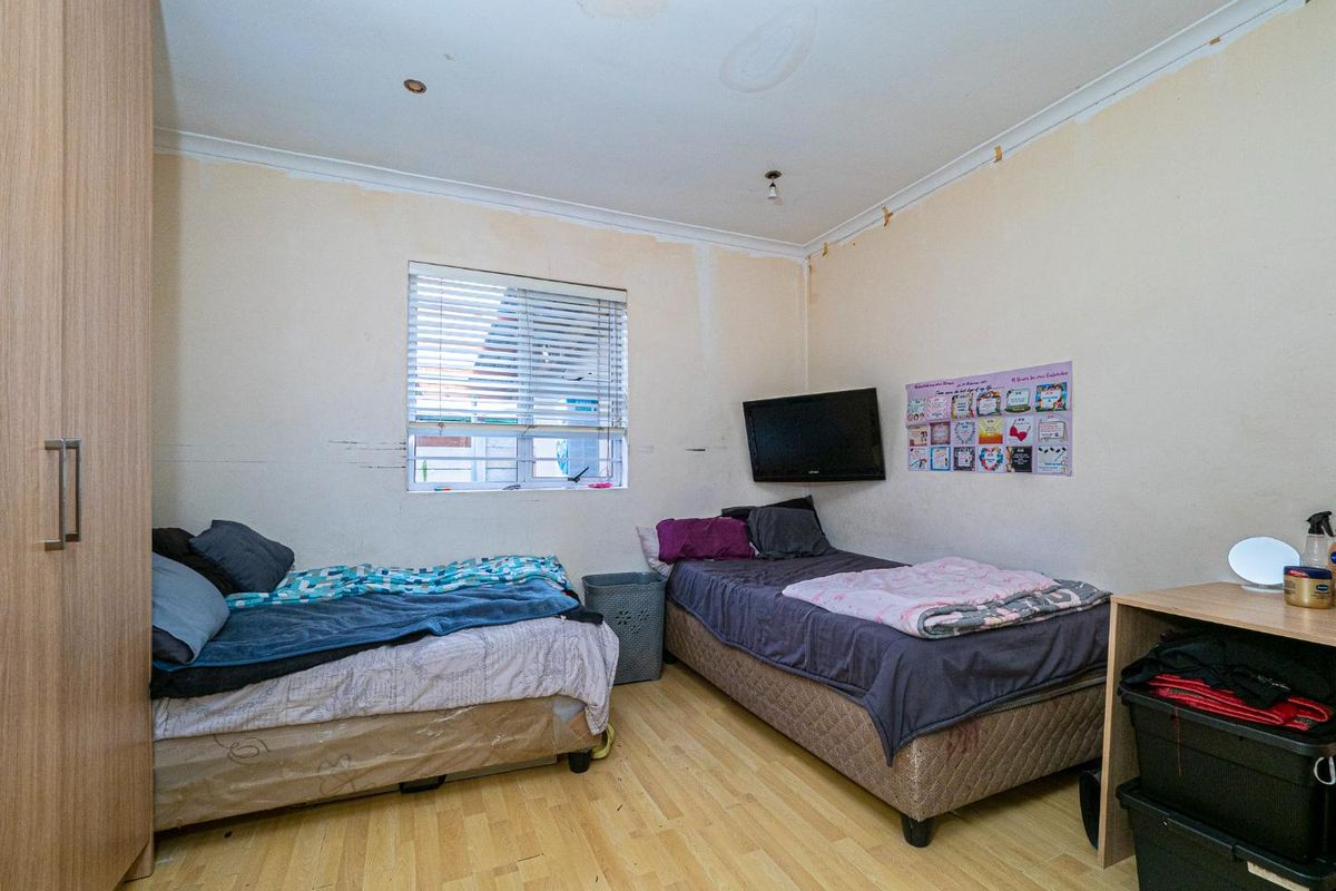 A bedroom featuring laminate flooring, a built-in wardrobe, and venetian blinds, currently showing signs of ceiling water damage and wall surface wear.