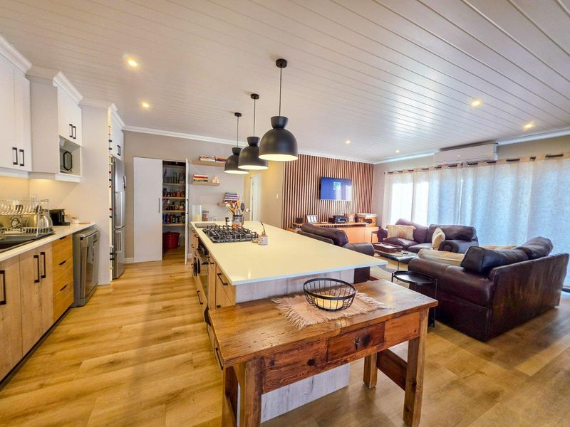 Spacious open-plan living area featuring a modern kitchen with a large island, gas cooktop, pantry, and a stylish slatted timber feature wall.