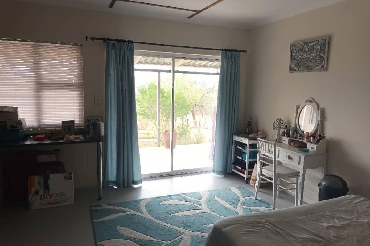 A bedroom featuring a sliding glass door with access to an outdoor area, neutral walls, and functional window treatments.