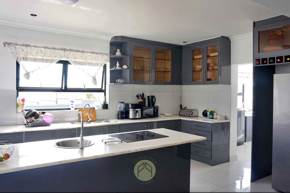 Modern kitchen featuring dark grey cabinetry, stone countertops, a central island with a built-in cooktop, and integrated storage solutions.