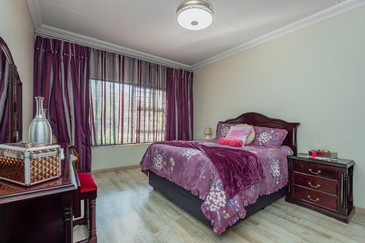 A well-maintained bedroom featuring light-toned wood-look flooring, crown molding, and a large window with floor-to-ceiling curtains.