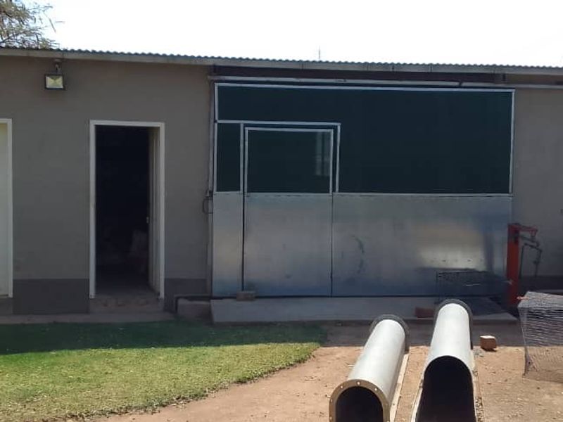 A utilitarian outbuilding featuring a metal sliding door, exterior lighting, and a simple plaster finish, situated in a garden setting.