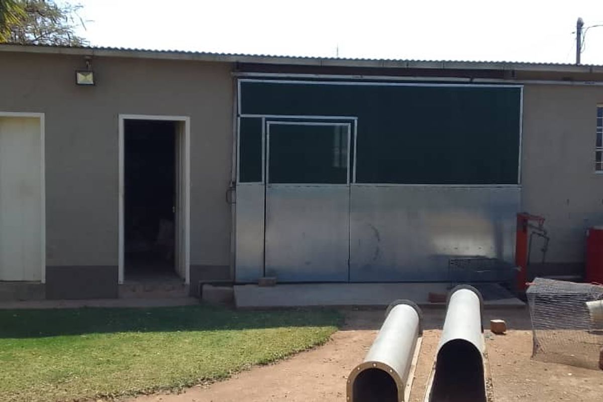 A utilitarian outbuilding featuring a metal sliding door, exterior lighting, and a simple plaster finish, situated in a garden setting.