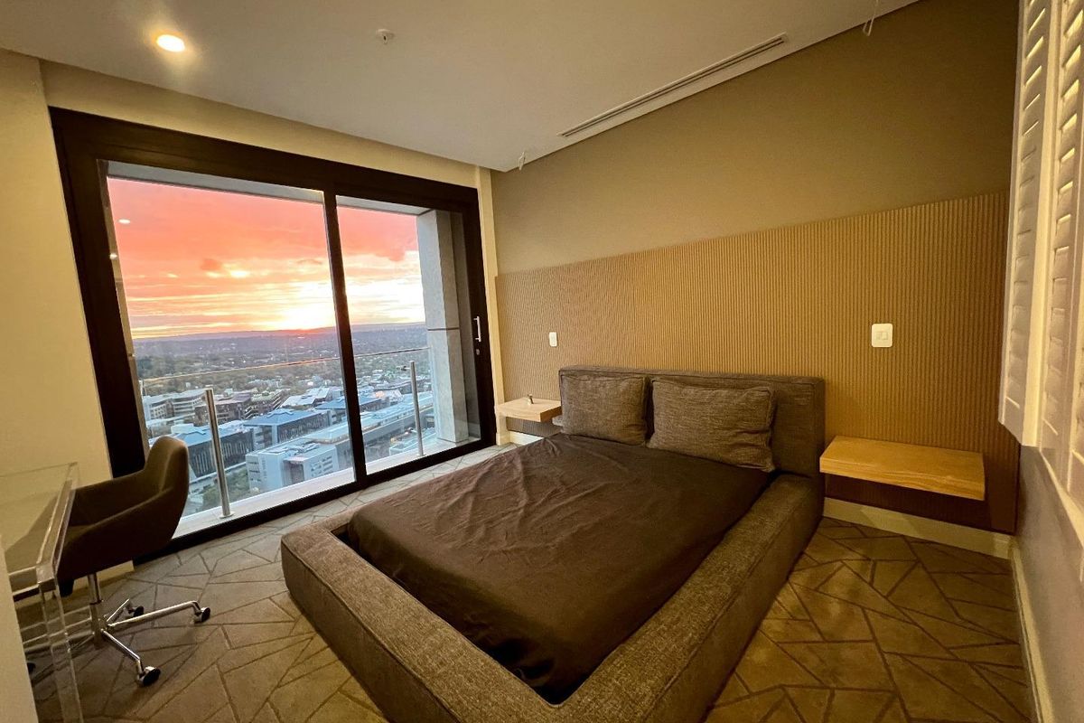 Modern bedroom featuring a large sliding glass door with sunset views, integrated wall paneling, and floating bedside tables.