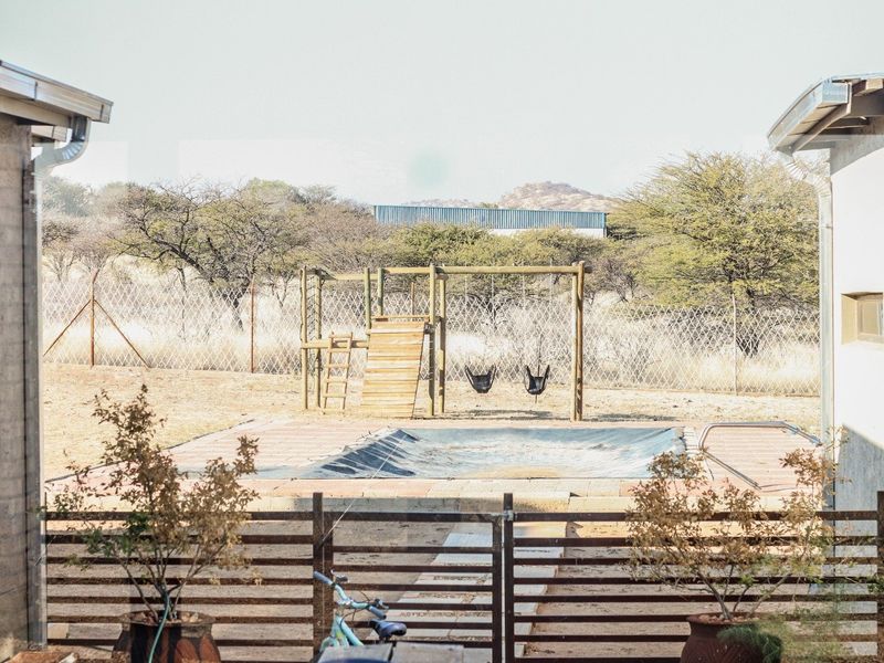 View of a backyard pool area featuring a pool cover, paved surround, and perimeter fencing, set against a natural landscape backdrop.