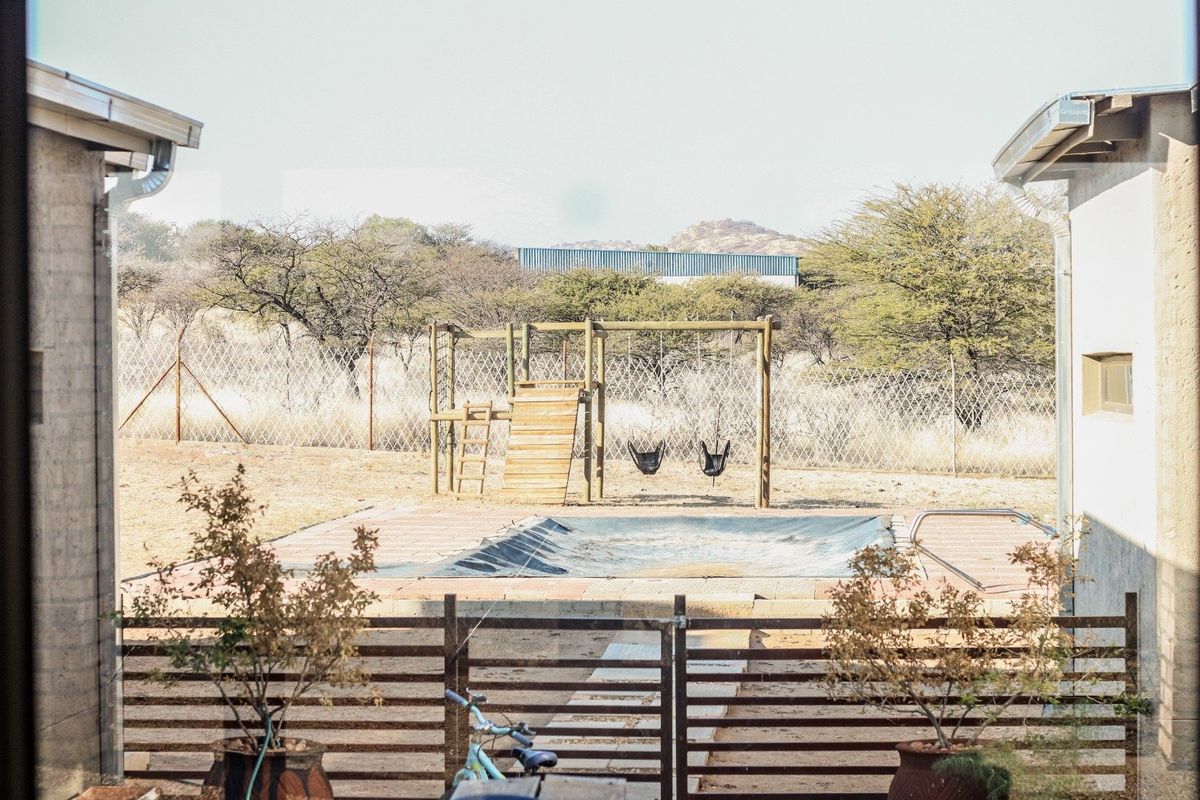 View of a backyard pool area featuring a pool cover, paved surround, and perimeter fencing, set against a natural landscape backdrop.