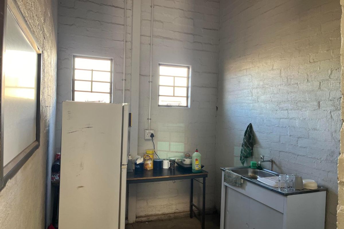 A basic utility kitchen area featuring exposed brick walls, a small sink unit, and functional window lighting.