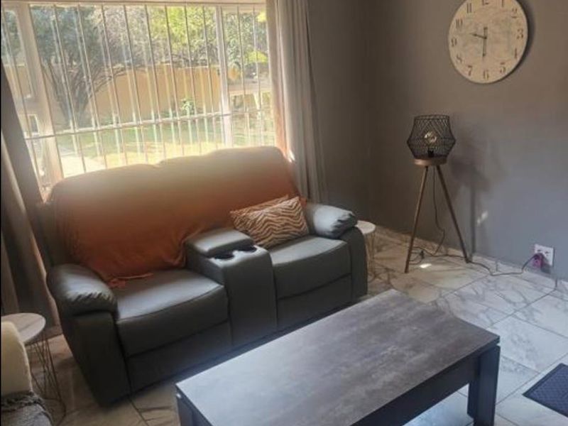 A living room featuring tiled flooring, neutral wall paint, and a large window fitted with security bars.