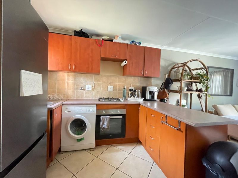 A functional kitchen featuring wooden cabinetry, tiled backsplash, gas hob, built-in oven, and a breakfast nook counter, with tiled flooring throughout.