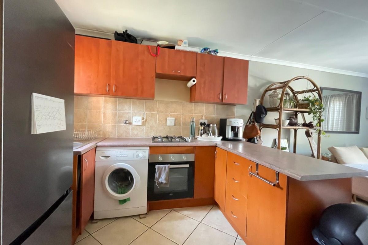 A functional kitchen featuring wooden cabinetry, tiled backsplash, gas hob, built-in oven, and a breakfast nook counter, with tiled flooring throughout.
