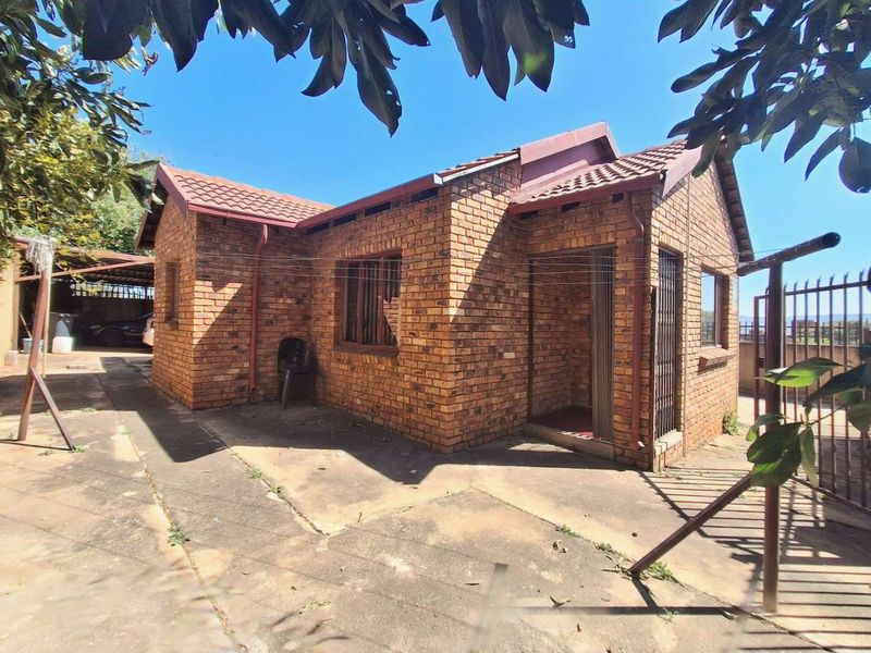 A single-story face-brick house featuring a tiled roof, concrete driveway, and security gate, set in a residential outdoor area.