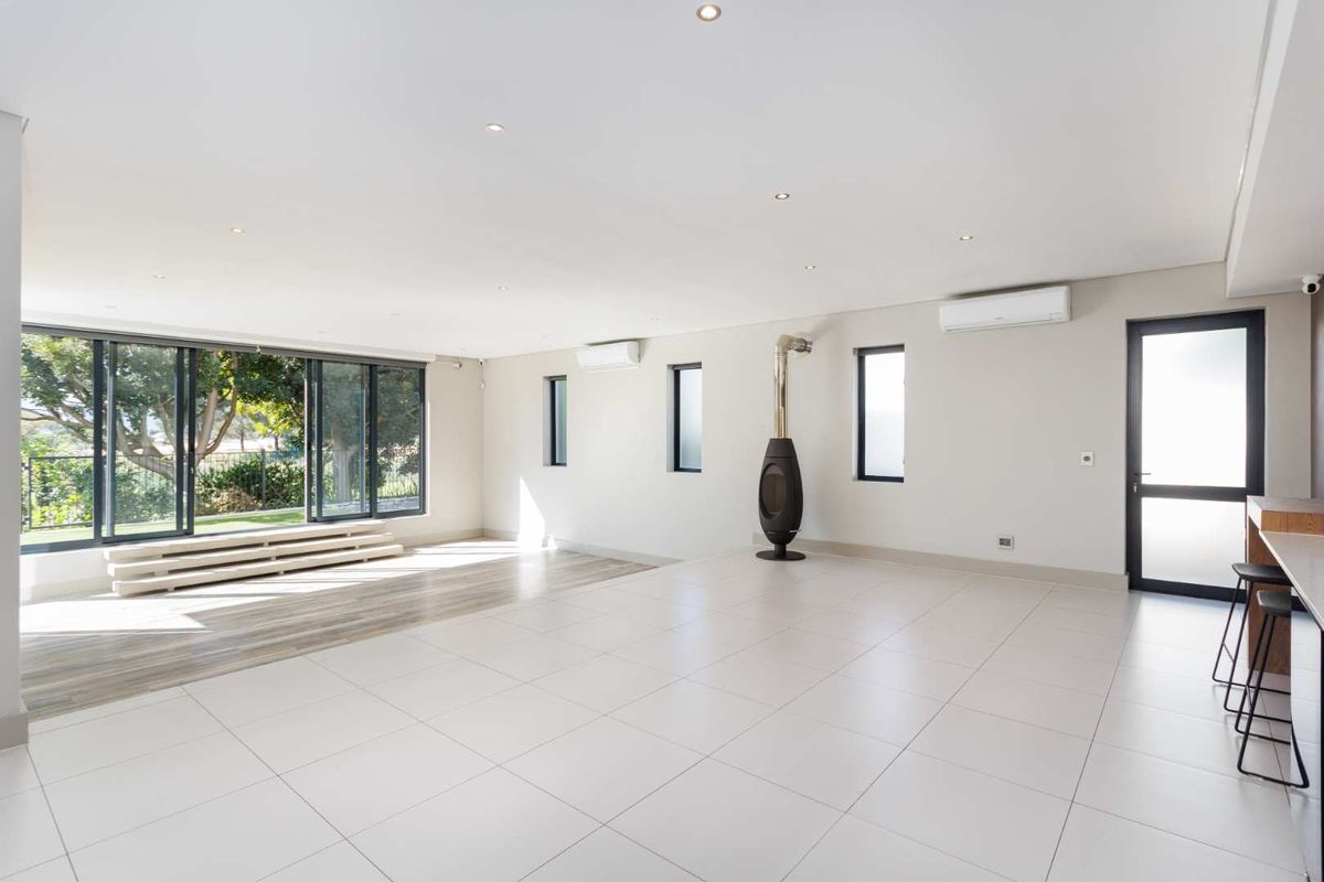 Spacious, light-filled living area featuring tiled floors, a modern freestanding fireplace, split-system air conditioning, and large sliding doors opening to the garden.