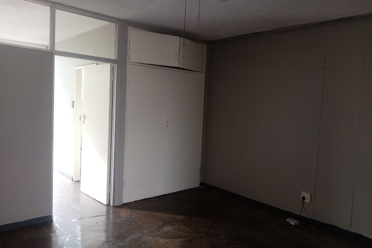 A vacant bedroom featuring built-in storage cupboards, a ceiling fan, and dark tiled flooring, with an adjacent doorway leading to another room.
