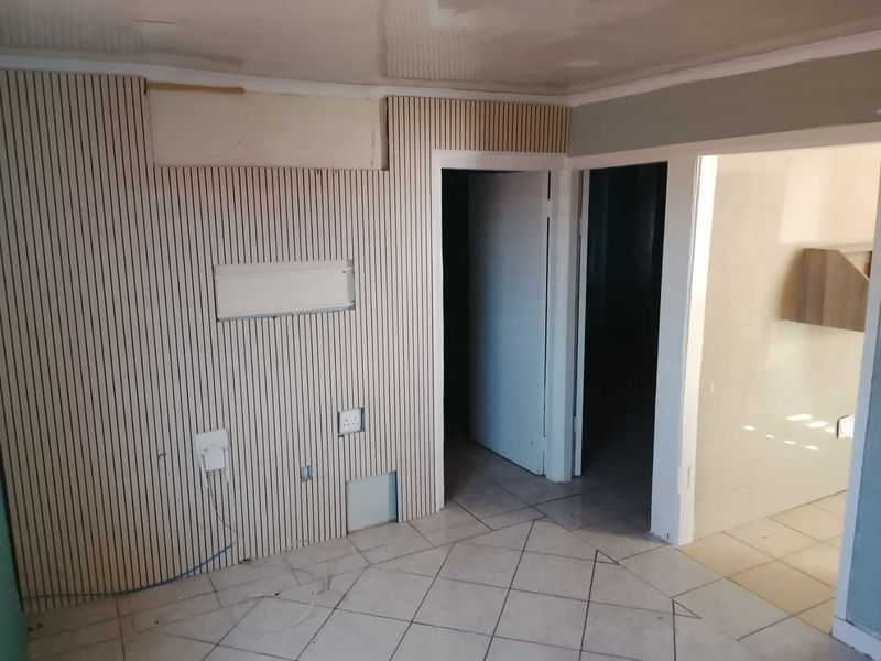 An empty living area featuring slatted wood wall paneling, tiled flooring, and coved ceilings, currently requiring finishing work on the wall surfaces.
