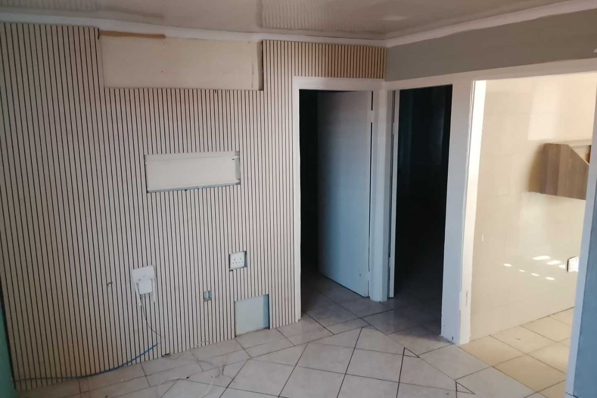 An empty living area featuring slatted wood wall paneling, tiled flooring, and coved ceilings, currently requiring finishing work on the wall surfaces.