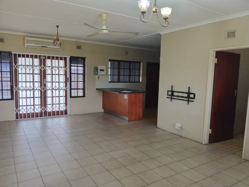 Spacious open-plan living area featuring tiled flooring, a breakfast bar, ceiling fan, and air conditioning unit, offering a versatile layout for modern living.