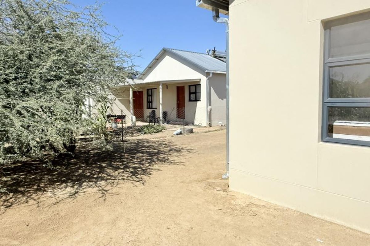 View of the rear exterior area showing a secondary building structure with a covered patio and sandy ground.