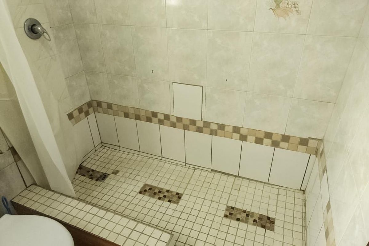 A bathroom shower area featuring tiled walls and flooring, currently showing signs of wear and missing tile sections requiring maintenance.
