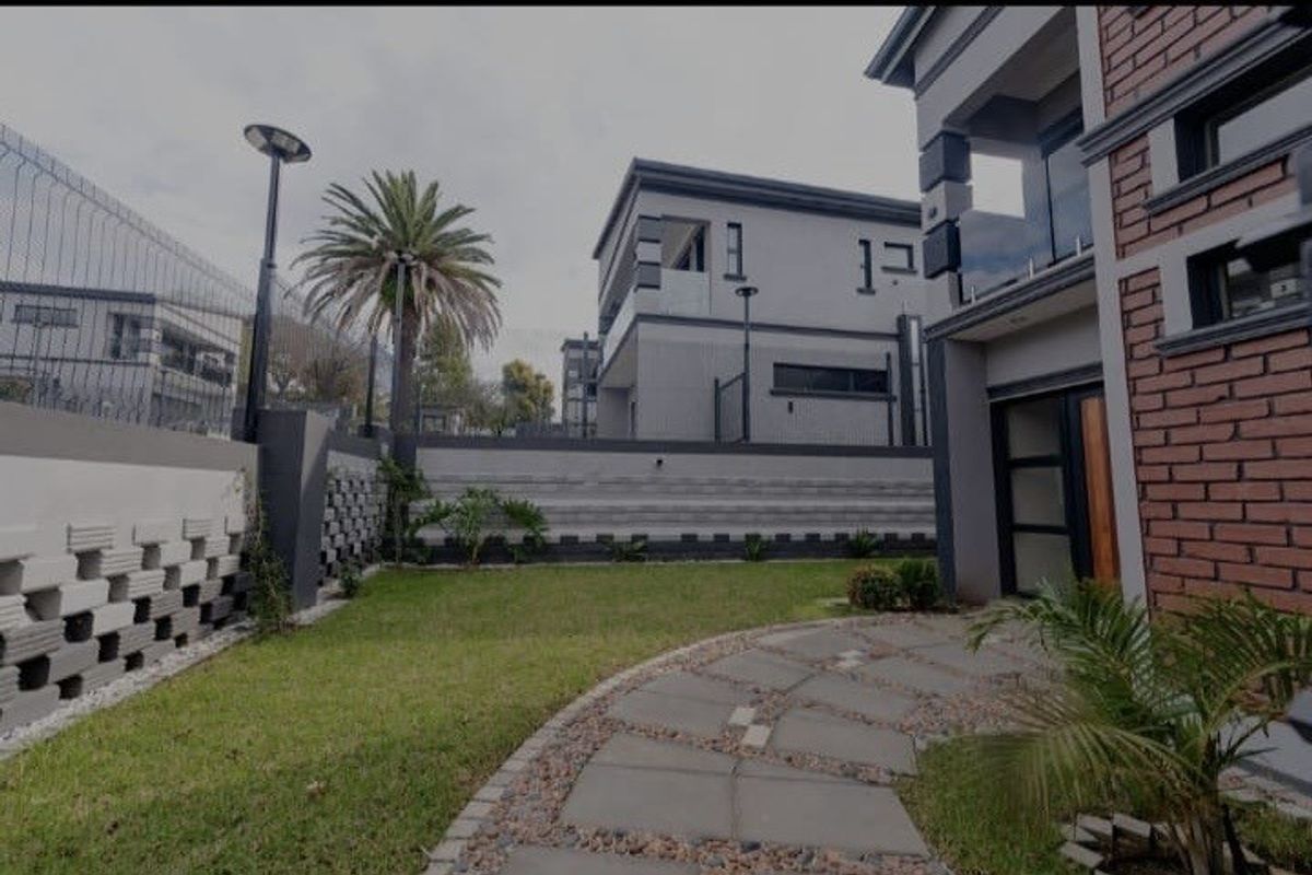 A well-maintained rear garden area featuring a paved walkway, brick and rendered facade, and secure boundary walling.
