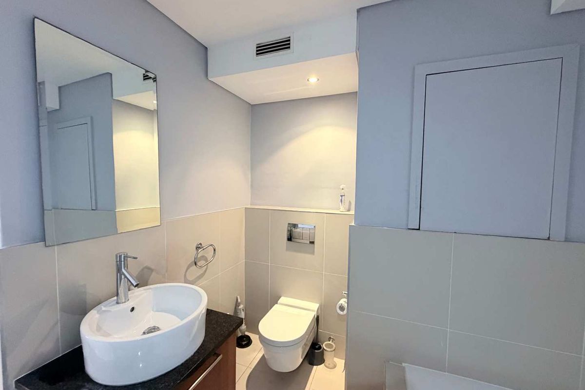A modern, well-maintained bathroom featuring a wall-mounted toilet, vanity cabinet with a countertop basin, and neutral tiled finishes.