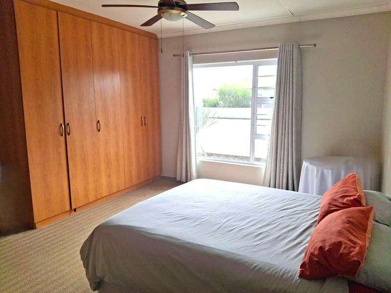 A well-maintained bedroom featuring extensive built-in wooden cupboards, a ceiling fan, and natural light through a large window.