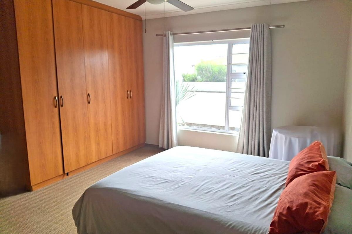 A well-maintained bedroom featuring extensive built-in wooden cupboards, a ceiling fan, and natural light through a large window.