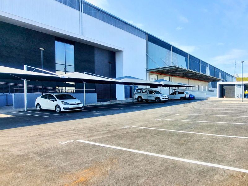 Modern industrial facility featuring a paved parking area with shade cloth carports and a large warehouse structure with a loading bay.